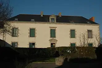 Vue d’un édifice à deux étages de cinq fenêtres, aux volets verts clos .