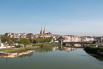 Vue d'un cours d'eau avec un pont à 3 arches, les flèches d'une cathédrale en arrière-plan.