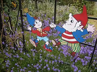 Deux figurines plates en acier à l'effigie des personnages de Oui-Oui et Potiron, ornant une grille dans un parc.