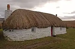 Photographie d'une maison aux murs blancs et au toit de chaume.