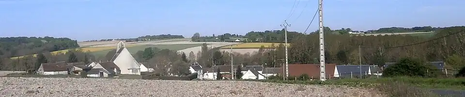 Photographie en couleur d'un alignement de maisons dont émerge le pignon d'une église moderne.