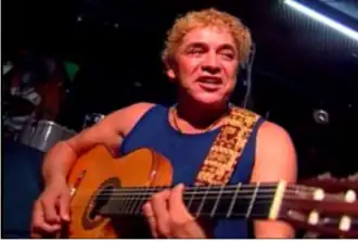 Un homme en débardeur bleu joue de la guitare.