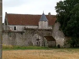 Vue générale d'un bâtiment dont la tourelle ronde dépasse d'un mur d'enceinte percé d'une porte cochère.