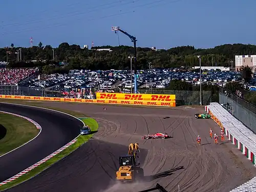 Photographie d'une monoplace verte dans un mur de pneus, d'une monoplace rouge proche d'une grue et de commissaires.