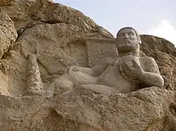 Statue taillée dans la roche représentant Héraclès nu reposant sur une peau de lion, une coupe à la main, au pied d’un olivier