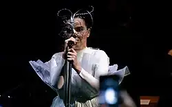 Image d'une chanteuse brune avec un masque et habillée de blanc