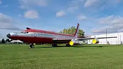Boeing 720 rouge et blanc, exposé sur une pelouse. Il a été modifié, il est doté d'un nez très long et quelques protubérences inhabituelles sont visibles sur le fuselage.