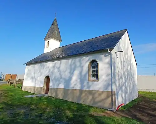 Vue latérale sud de la chapelle et son chevet à l'est. Le mur antibruit au nord de la parcelle marque la séparation avec la ligne de chemin de fer de Nantes à Saint-Nazaire, dévoyée à compter du 7 octobre 2022 pour contourner la raffinerie de Donges.