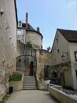 Photographie en couleurs d'un chemin bitumé longeant des structures urbaines et passant sous une arcade.
