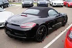Photo d'une Boxster GTS vu de 3/4 arrière sur un parking, avec une capote et des jantes Carrera S noires.