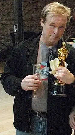 Le réalisateur américain Brad Bird tenant un verre de champagne d'une main et un Oscar de l'autre.