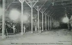 Carte postale ancienne en noir et blanc représentant des personnages dans un bâtiment agricole.