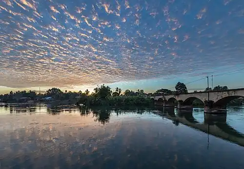 Pont vers Don Khon vu depuis Don Det avec le reflet dans l'eau du Mékong de nuages orange filandreux au lever du soleil, à Si Phan Don, Laos.