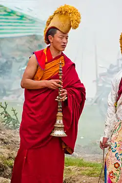 Photographie en couleurs d'un moine bouddhiste portant un kesa rouge et coiffé d'un bonnet jaune.