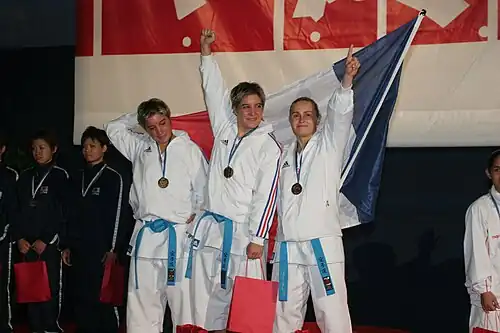 L'équipe de France de kata féminin victorieuse aux championnats du monde de karaté seniors 2006. À gauche : Jessica Buil. Au milieu : Sabrina Buil. Sabrina Buil, au centre, brandit le poing d'un air victorieux.