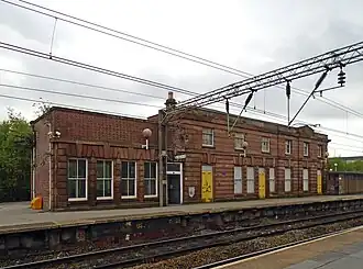 Bâtiment voyageur en briques rouges, le long d'un double quai traversé par deux voies électrifiées