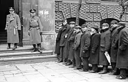 Grande file d'attente de Juifs pour l'enregistrement au travail forcé du ghetto, devant l'ancienne école de commerce, à l'intersection de la rue Prosta avec Waliców, qui abrite alors différentes institutions gouvernementales (mai 1941)