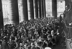 Photo en noir et blanc montrant une foule d'hommes serrés sous un porche à haute colonnes