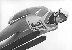 Photographie en noir et blanc d'un sauteur à ski en vol, portant un casque, des lunettes et un dossard avec le no&nbsp;35.