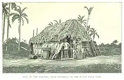 Photo en noir et blanc d'un couple et son enfant devant une cabane au toit en feuilles de palmier