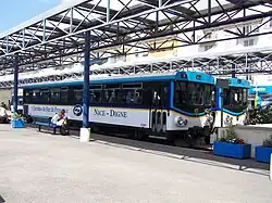 Vue de deux bus en gare routière sous une structure métallique avec le quai en premier plan.