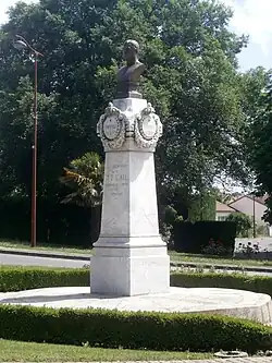 Photographie en couleurs d'un buste en métal sur un piédestal de pierre.