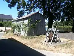 Photographie en couleurs d'une cabane en planche à côté de laquelle se trouve le tambour d'un treuil.