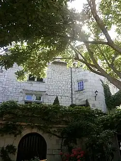 Photogtraphie en couleurs d'un b^^atiment pourvu d'une tourelle partiellement masqué par la végétation d'une cour.