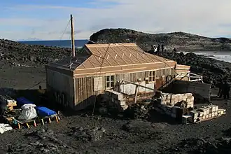 Cabane entourée de nombreuses caisses et matériaux divers sur un cap rocheux.