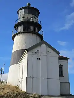 Photo en très gros plan du phare, légère contre-plongée. La peinture du bâtiment semble propre sans être neuve, avec quelques traces de rouille au niveau de la rambarde.