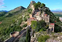 Château en pierre sur une colline arborée.