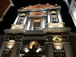 Vue en contre-plongée de nuit d'une façade savamment éclairée de type baroque possédant fronton, décorations et statues.