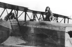 Photo noir et blanc d'un homme en tenue de vol, debout dans le fuselage d'un avion, à la place du mitrailleur (derrière le poste de pilotage).