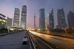 Gratte ciel illuminés de nuit. Au milieu, une autoroute contrebalance la verticalité des bâtiments.