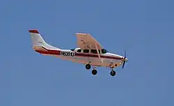 Vue par le côté droit, légèrement en dessous, d'un petit avion de tourisme blanc et rouge, en phase d'approche pour l'atterrissage, avec les volets sortis.