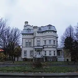 La façade d'un bâtiment de trois étages, de plan complexe, revêtue de briques de couleur beige.
