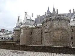 Photographie en couleurs des remparts et des tours d'un château en pleine ville.