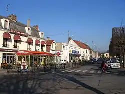 Photographie d'une place urbaine, bordée par des commerces.