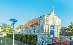 Photo en couleur montrant un bâtiment en pierres, surmonté d'une croix, avec un toit en tuiles.