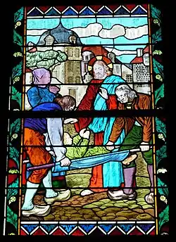 Vitrail avec quatre personnages, une construction en arrière-plan, ciel bleu.