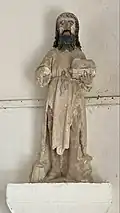 photo en couleurs de la statue de saint Jean-Baptiste sur un socle blanc fixé au mur.