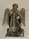 photo en couleurs de la statue de saint Michel sur un socle blanc fixé au mur.