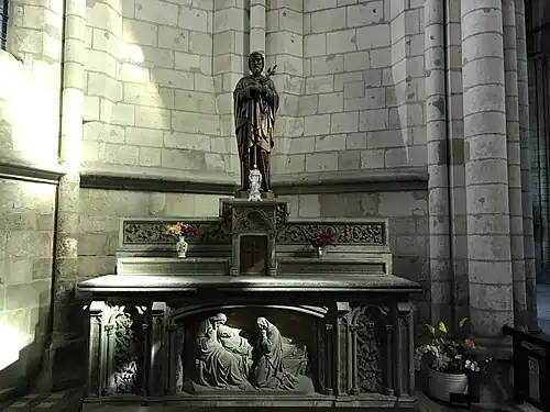 Autel présentant, en bas de l'image, un bas-relief représentant un homme et une femme pleurant autour d'un corps. Sur l'autel, deux statues d'hommes barbues et quelques pots de fleurs.