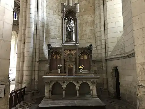 Autel présentant des petites murailles sculptées et surmontée d'une femme vêtue de bleu et apprenant à une petite fille à lire.