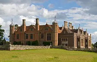 Photo d'un grand bâtiment en briques rouges flanqué de plusieurs tours et entouré d'une pelouse verte