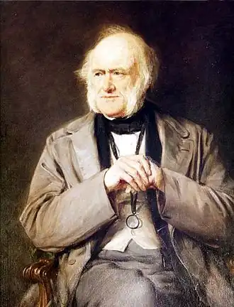 Portrait à l’huile. Lyell, au crâne fort dégarni mais portant de longs favoris blancs, est assis dans un fauteuil, les coudes posés sur les accoudoirs, mains croisées devant lui à hauteur de la poitrine. Il regarde légèrement sur sa droite.