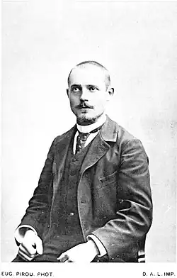 Photographie monochrome d'un homme assis, de face.