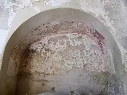 Photographie en couleurs d'une niche dans un mur dont la voûte porte des vestiges de peinture rouge foncé.