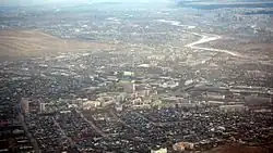 Photographie aérienne d'une grande zone urbanisée depuis un avion. Au centre se trouvent des immeubles tandis qu'autour se trouvent de vastes zones de maisons. Une rivière coule dans le coin en haut à droite de la photographie.