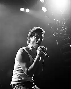 Photographie en noir et blanc d'un homme debout sur scène chantant dans un micro.